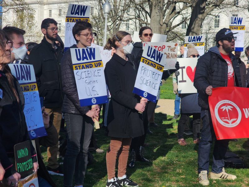 Unionized federal workers and their supporters stand together holding signs saying “Protect Science” and “Science Serves U.S.” at the Kill the Cuts rally in Washington DC on April 8, 2025. Photo by Maximillian Alvarez.