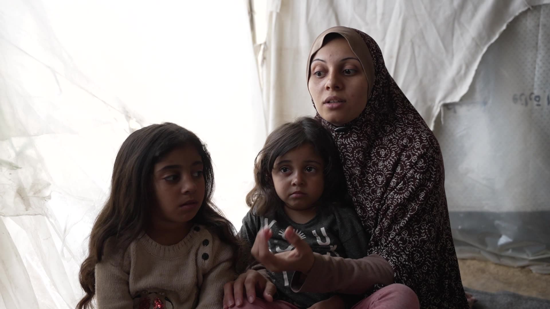 Sabreen al Masri holds her two children inside a tent. Still from video by Ruwaida Amer and Mahmoud Al Mashharawi
