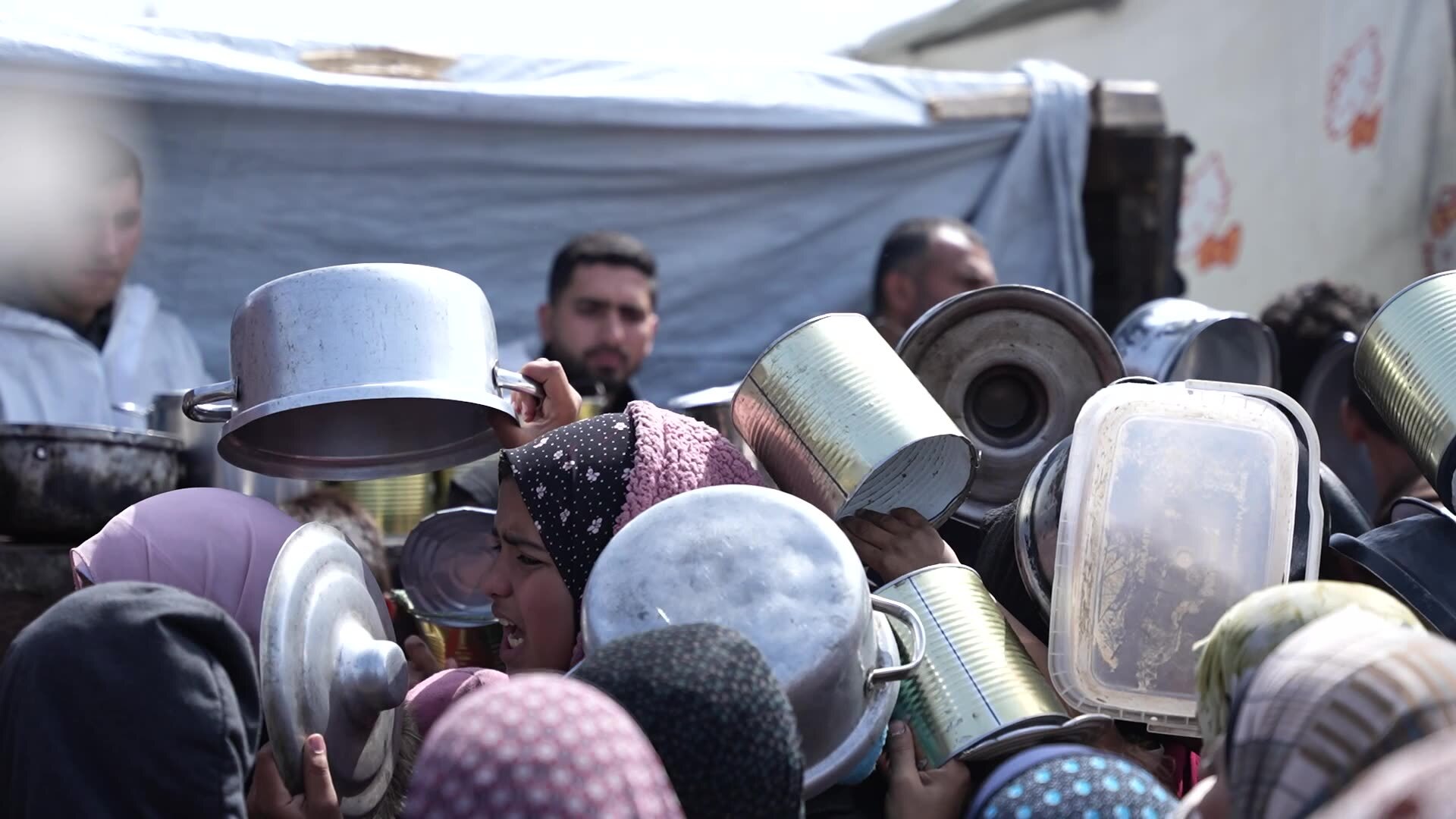 A crowd gathers in front of a grocery seller, holding pots and pans. Prices in Gaza have skyrocketed, with a single bag of flour going for as much as $200 USD. Screenshot from video by Ruwaida Amer and Mahmoud Al Mashharawi
