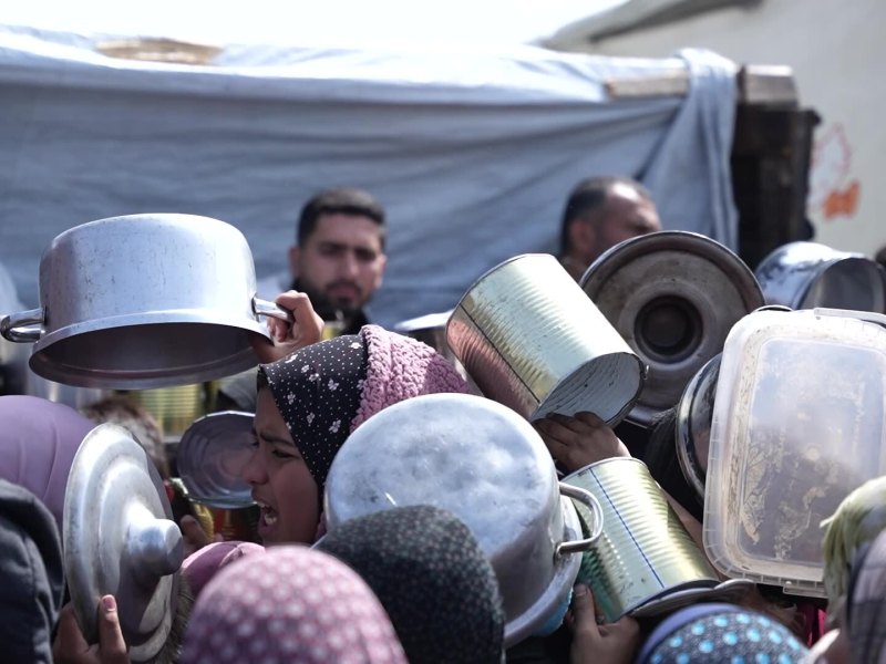 A crowd gathers in front of a grocery seller, holding pots and pans. Prices in Gaza have skyrocketed, with a single bag of flour going for as much as $200 USD. Screenshot from video by Ruwaida Amer and Mahmoud Al Mashharawi
