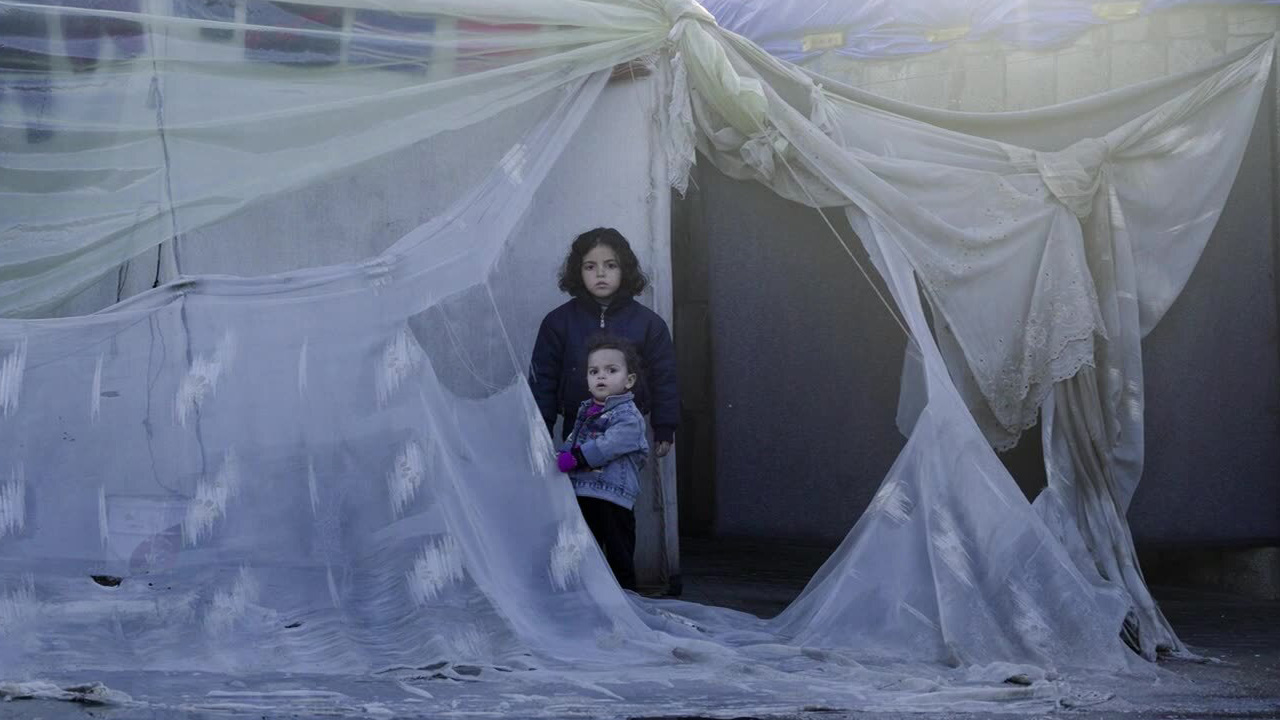 Two girls gaze out from a tent in Gaza.