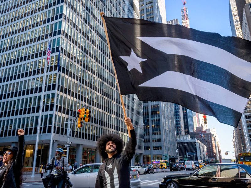 Protester holding a black Puerto Rican flag, a symbol of the mourning of the Puerto Rican Nation in colonial captivity. Photo by Erik McGregor/LightRocket via Getty Images