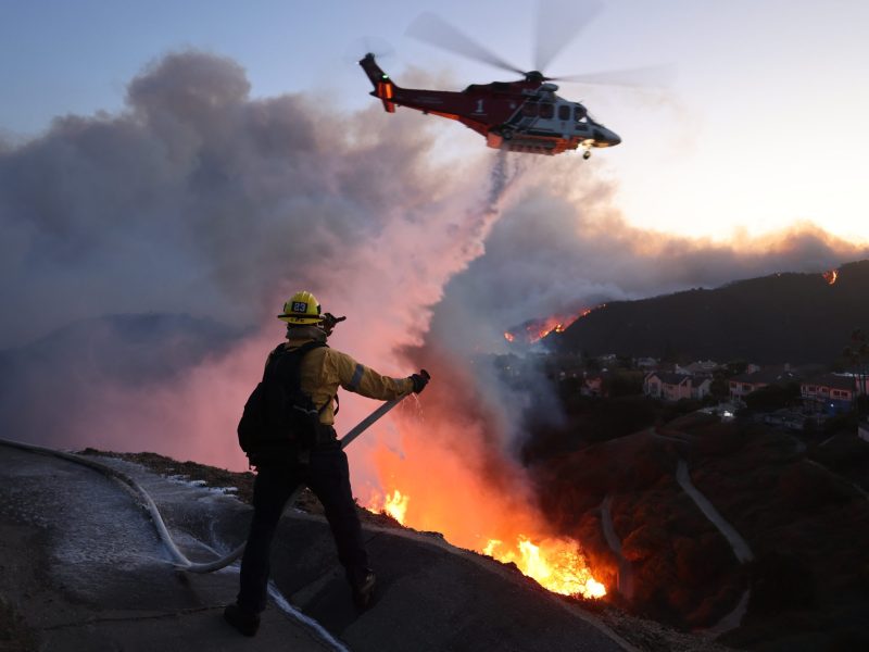 Fire personnel respond to homes destroyed while a helicopter drops water as the Palisades Fire grows in Pacific Palisades, California on January 7, 2025. Photo by DAVID SWANSON/AFP via Getty Images