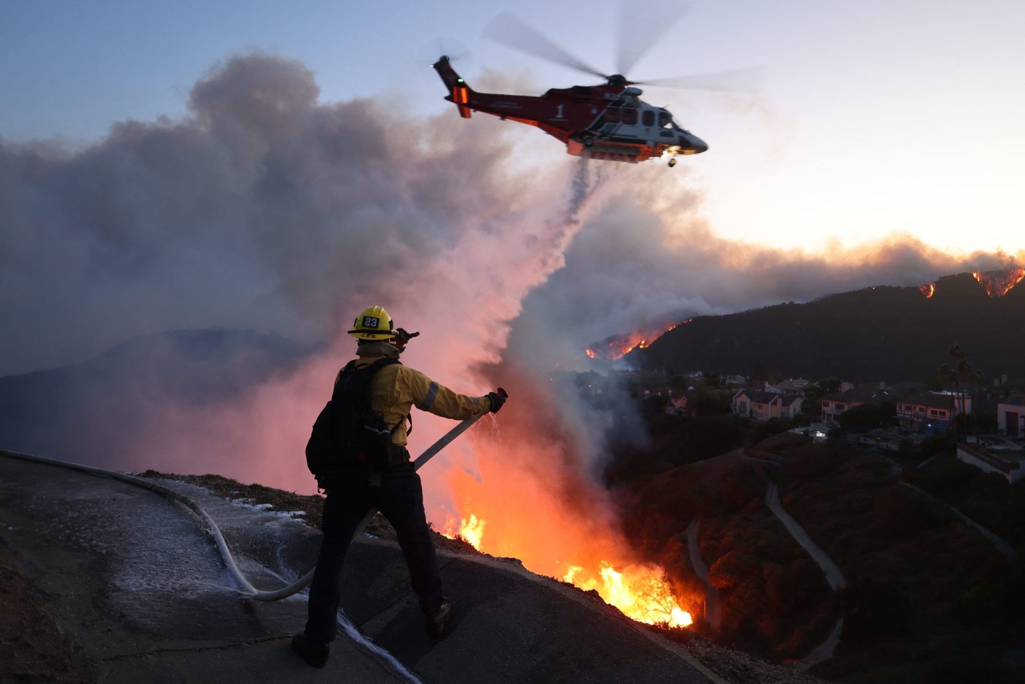 Fire personnel respond to homes destroyed while a helicopter drops water as the Palisades Fire grows in Pacific Palisades, California on January 7, 2025. Photo by DAVID SWANSON/AFP via Getty Images