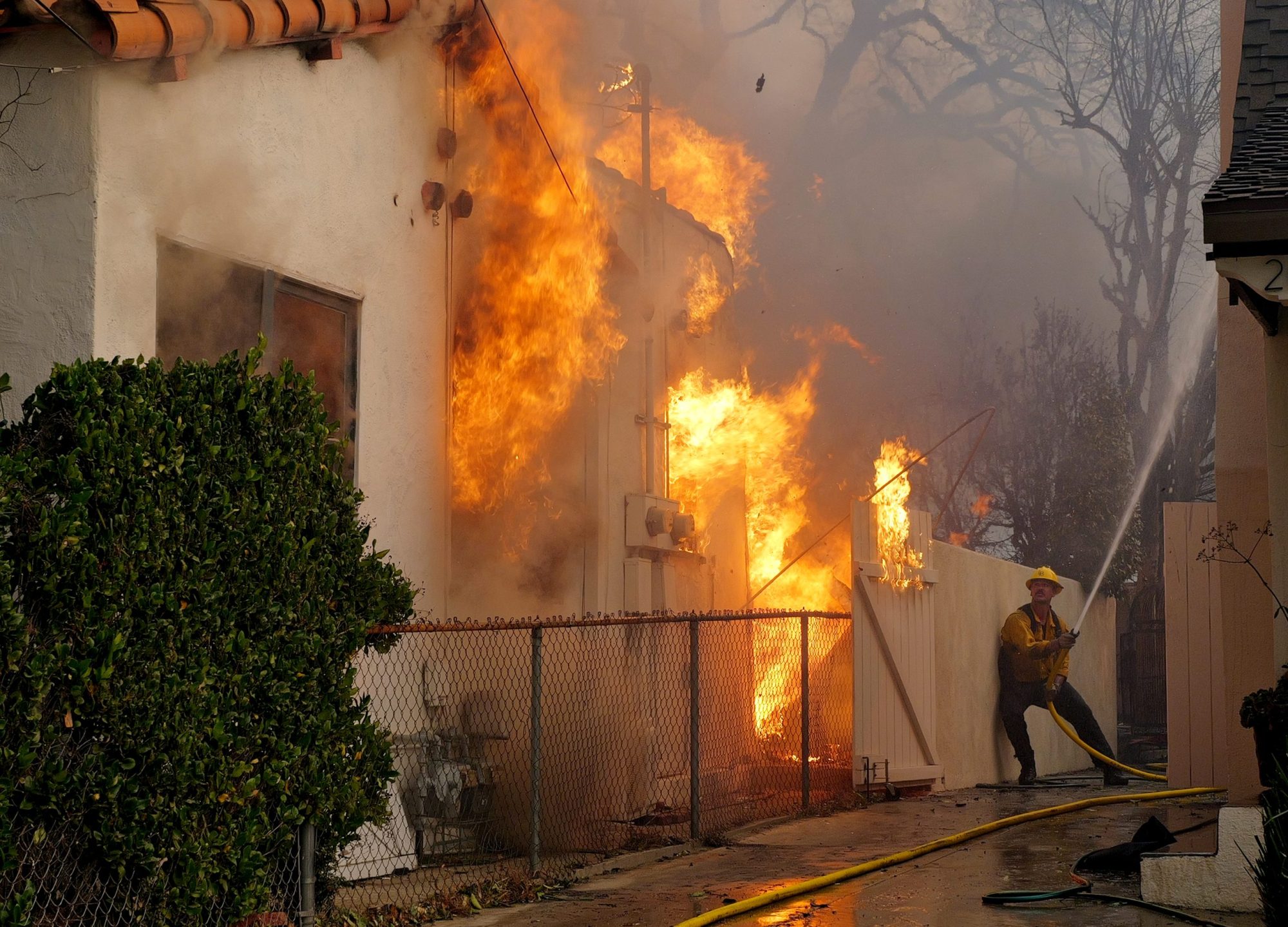 A firefighter sprays water on a house to protect it from the Eaton Fire in the Altadena neighborhood on January 08, 2025. Photo by Nick Ut/Getty Images